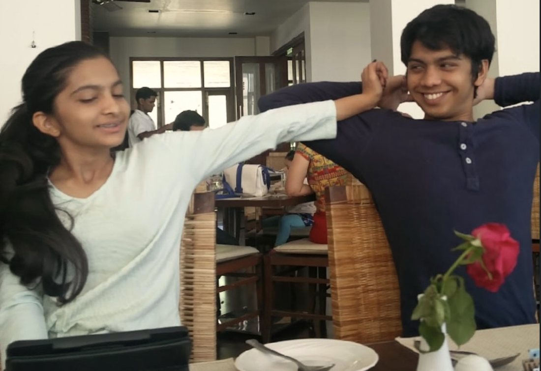 Anoushka and Rohan laughing together at a table, arms raised